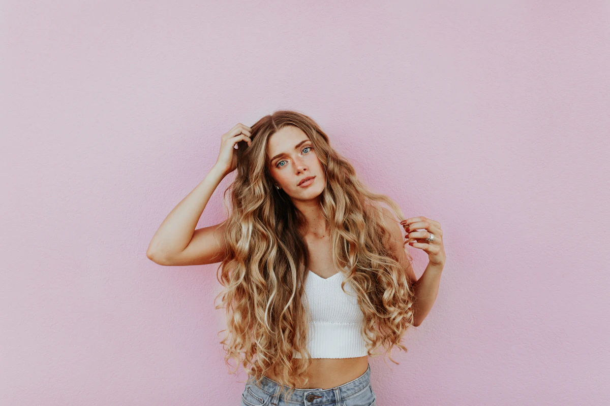 Woman with long wavy hair against a pink wall