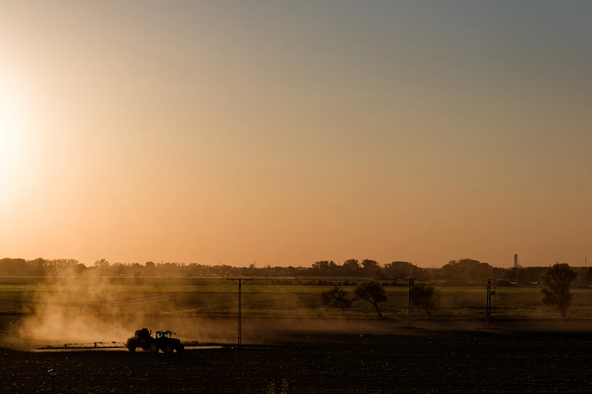 Tractor driving through a dusty field at sunset
