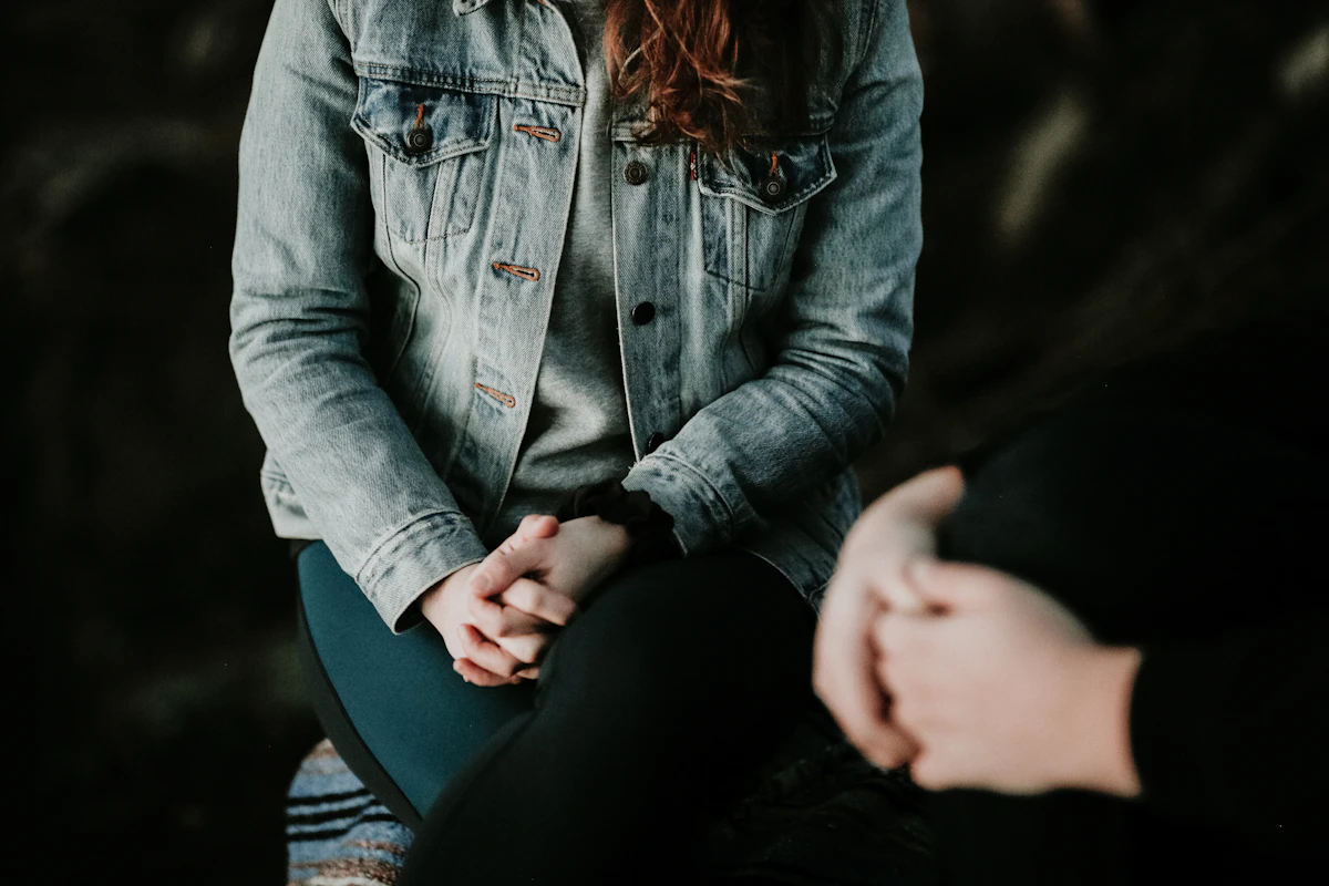 Woman in a denim jacket sitting, hands folded