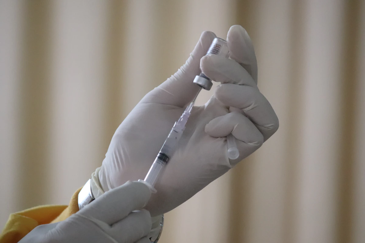 A person in white latex gloves drawing liquid from a vial into a syringe