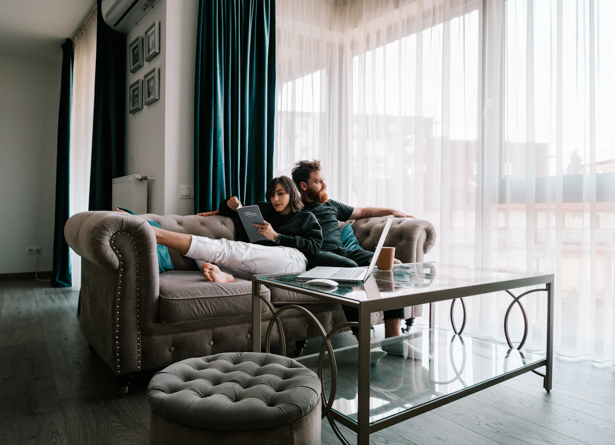 Two people relaxing on a sofa near a window