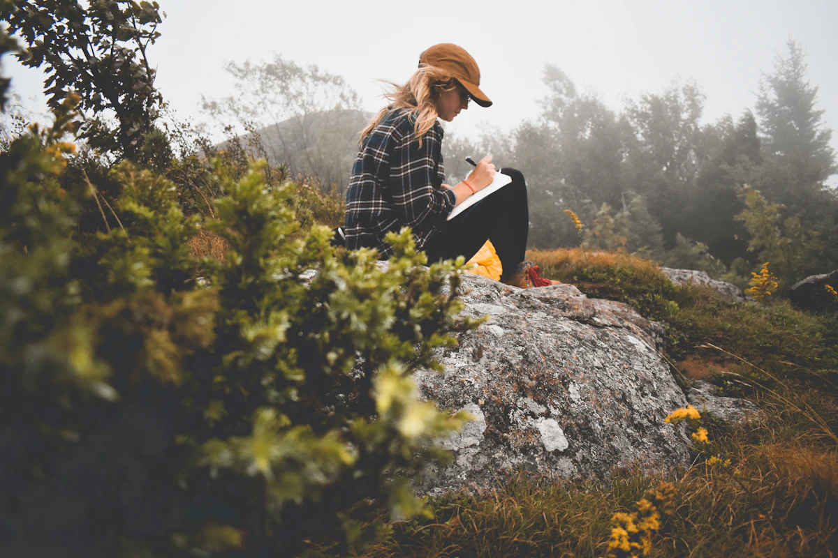 A woman sitting on top of a rock writing in a journal