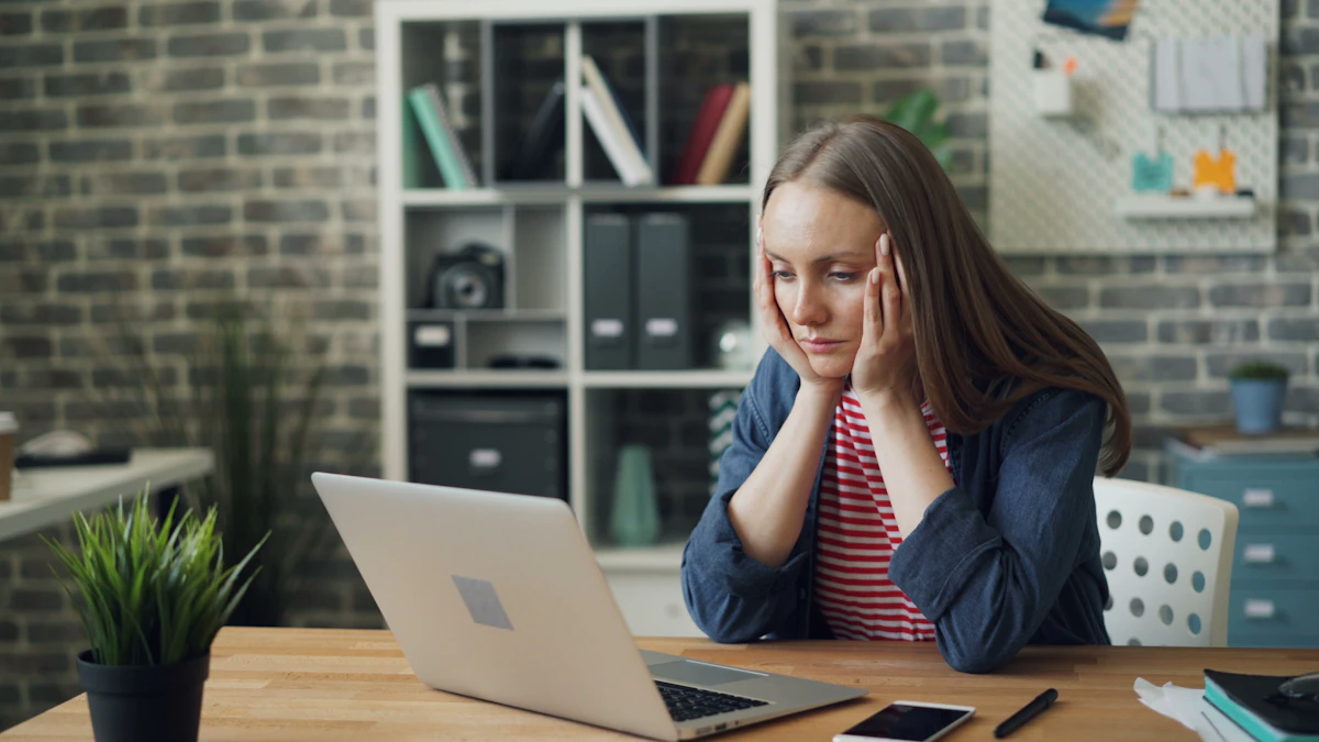 A woman sitting at a table with a laptop, looking tired