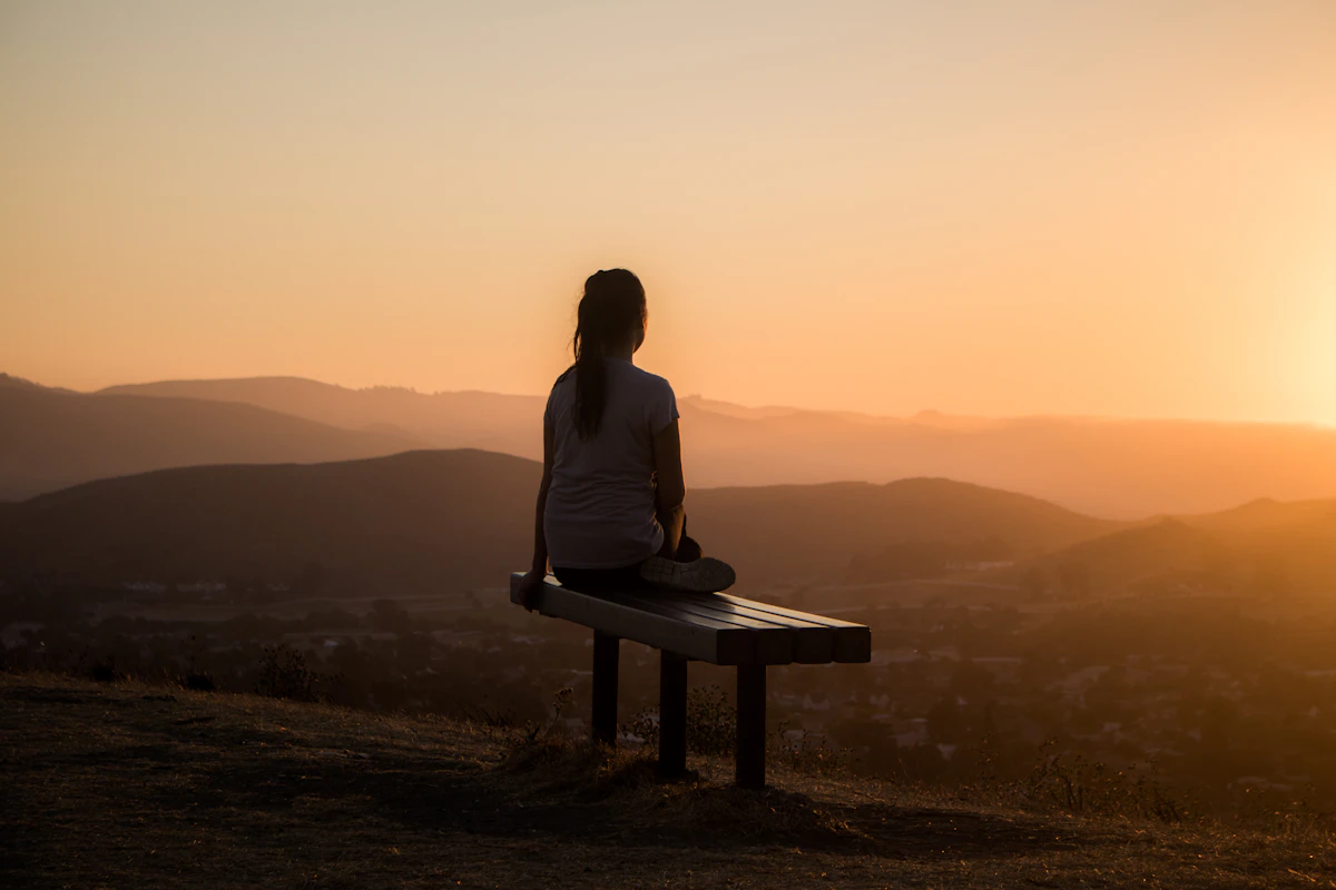 Woman sitting on a bench overlooking the mountains at sunset