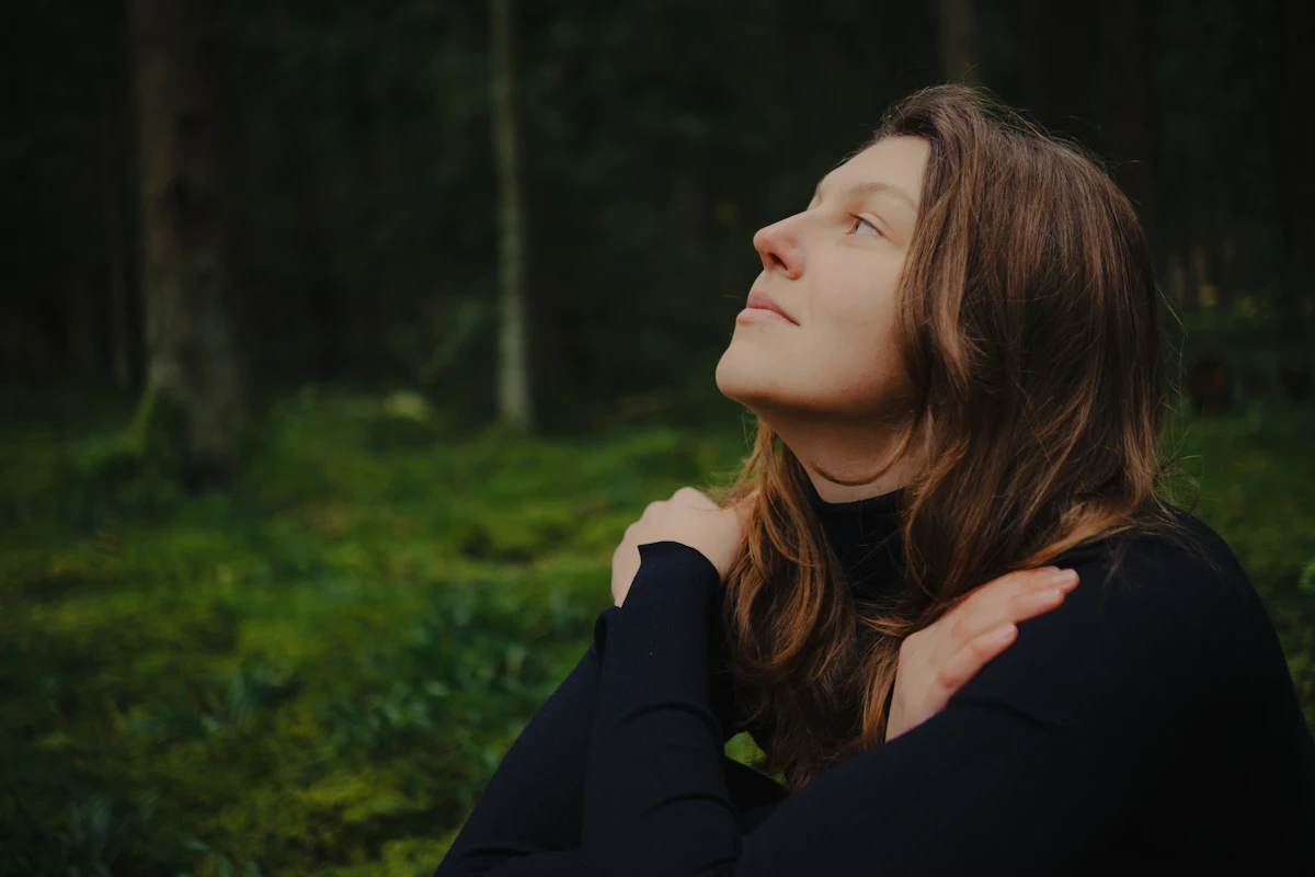 Woman with eyes closed embracing herself in the forest
