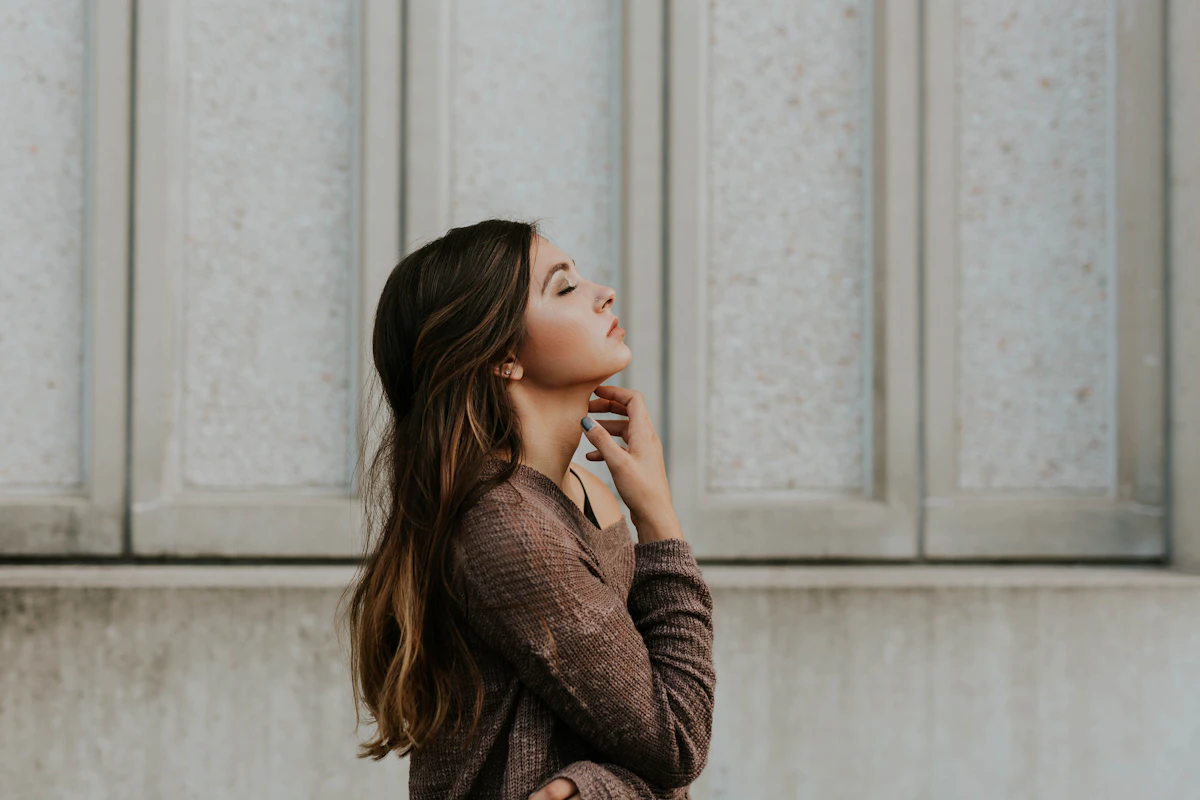 Woman in a brown top standing beside a wall, thinking